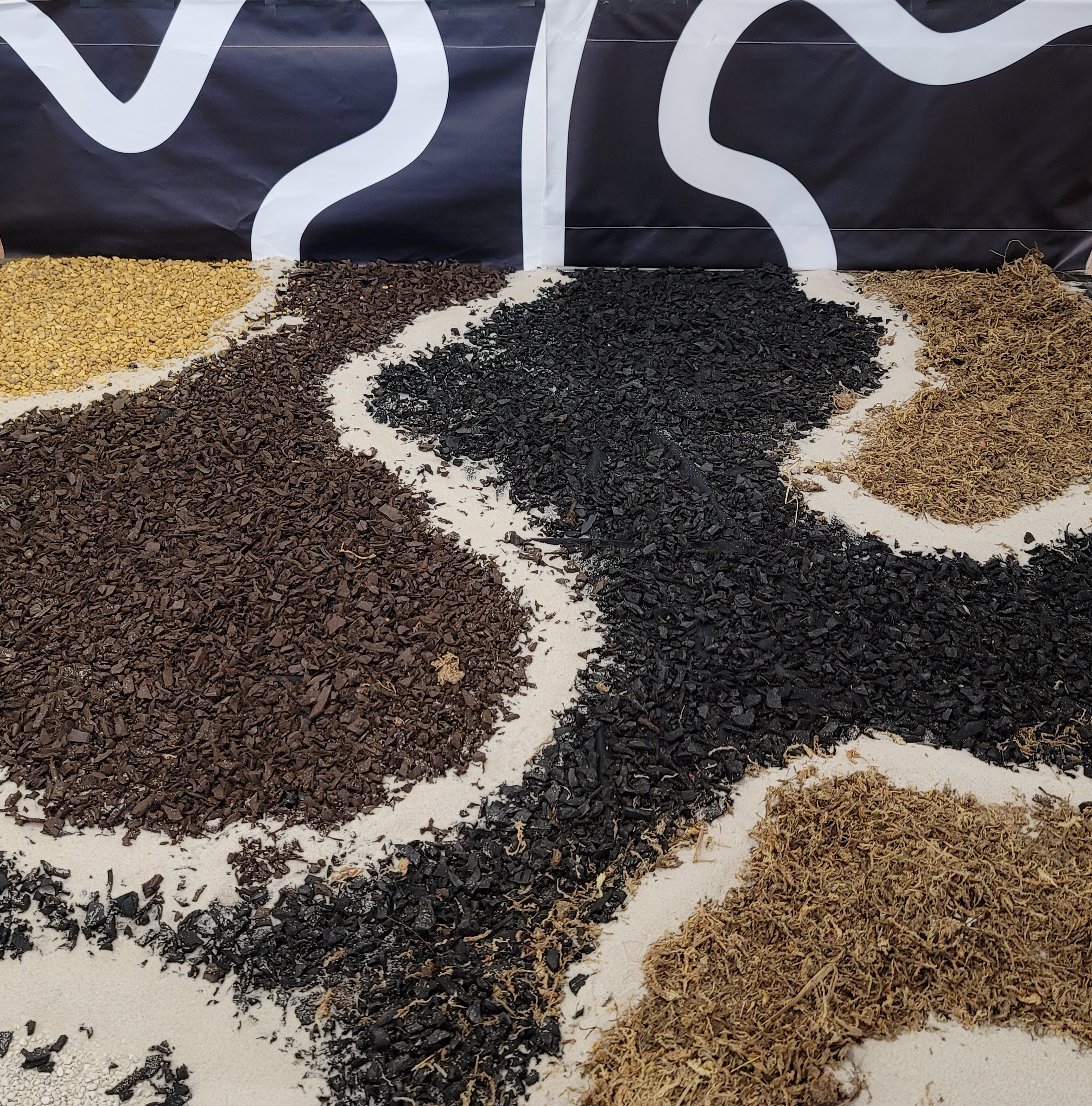 On the ground is a variety of media such as mulch, sphagnum moss, sand, and gravel. White lines of sand snake through the piece, and connect with lines on a vertical printed portion of the piece. This image only shows a portion of the artwork.